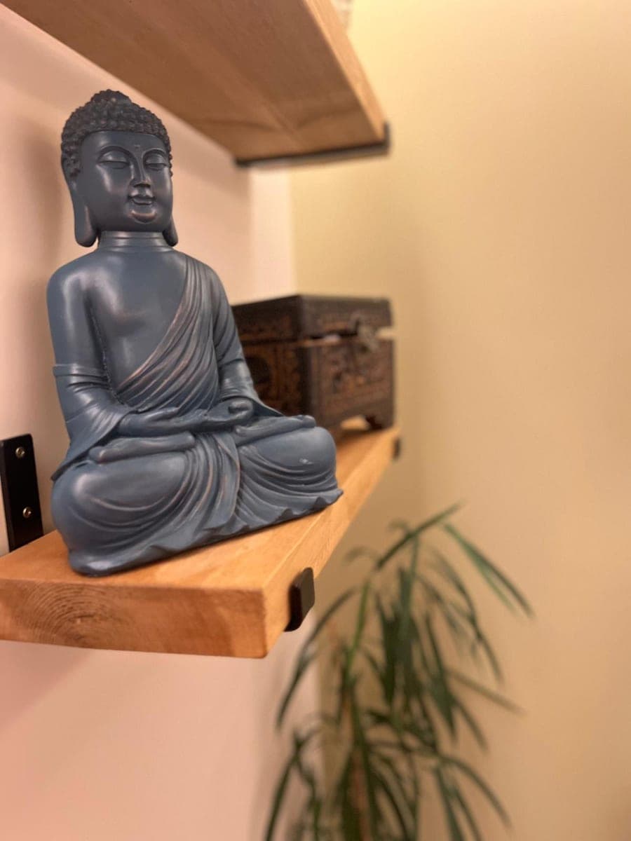 A dark grey Buddha figure and a plant on a floating oak shelf in the treatment room.