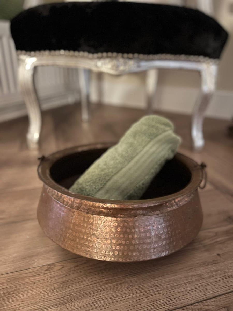 A copper foot bath with a folded green towel, ready for the optional foot soak on arrival.