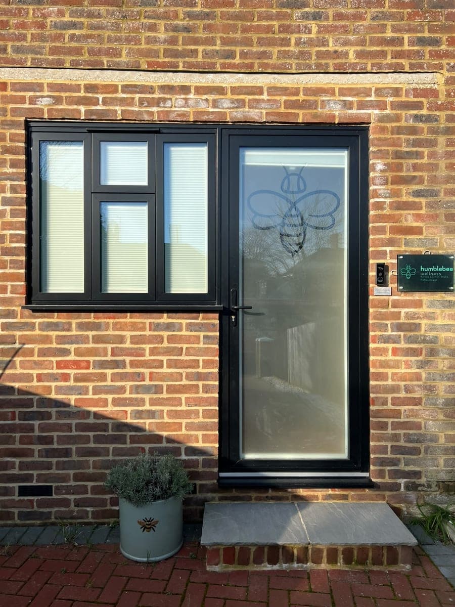 The entrance at 33 The Green: a black-framed door with the Humblebee bee on the glass, a small sign beside it and lavender in a planter.