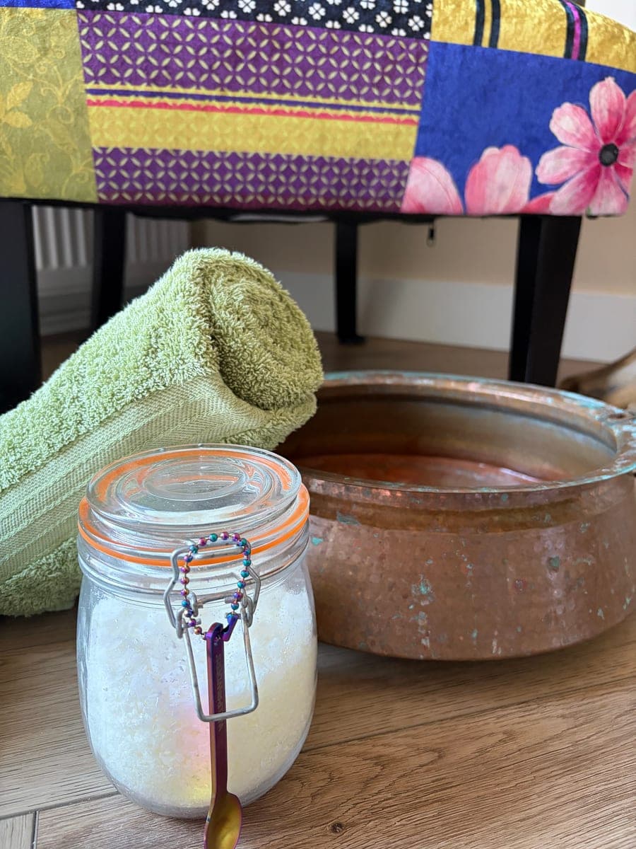 The copper foot bowl with a rolled green towel, beside a glass jar of foot-soak salts with a little scoop.