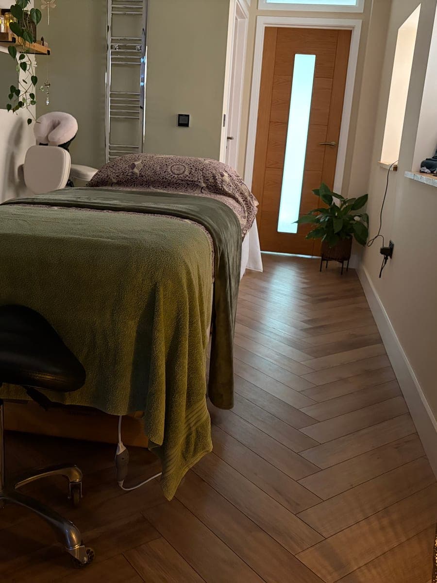 The whole treatment room: the made-up couch and stool, with a lamp and plants, and the door at the far end.