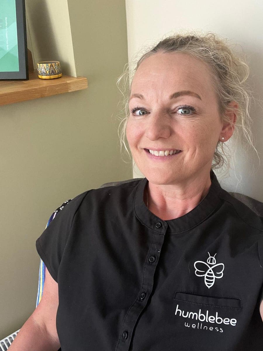 Kirstie, smiling, in a black Humblebee Wellness tunic in the treatment room.